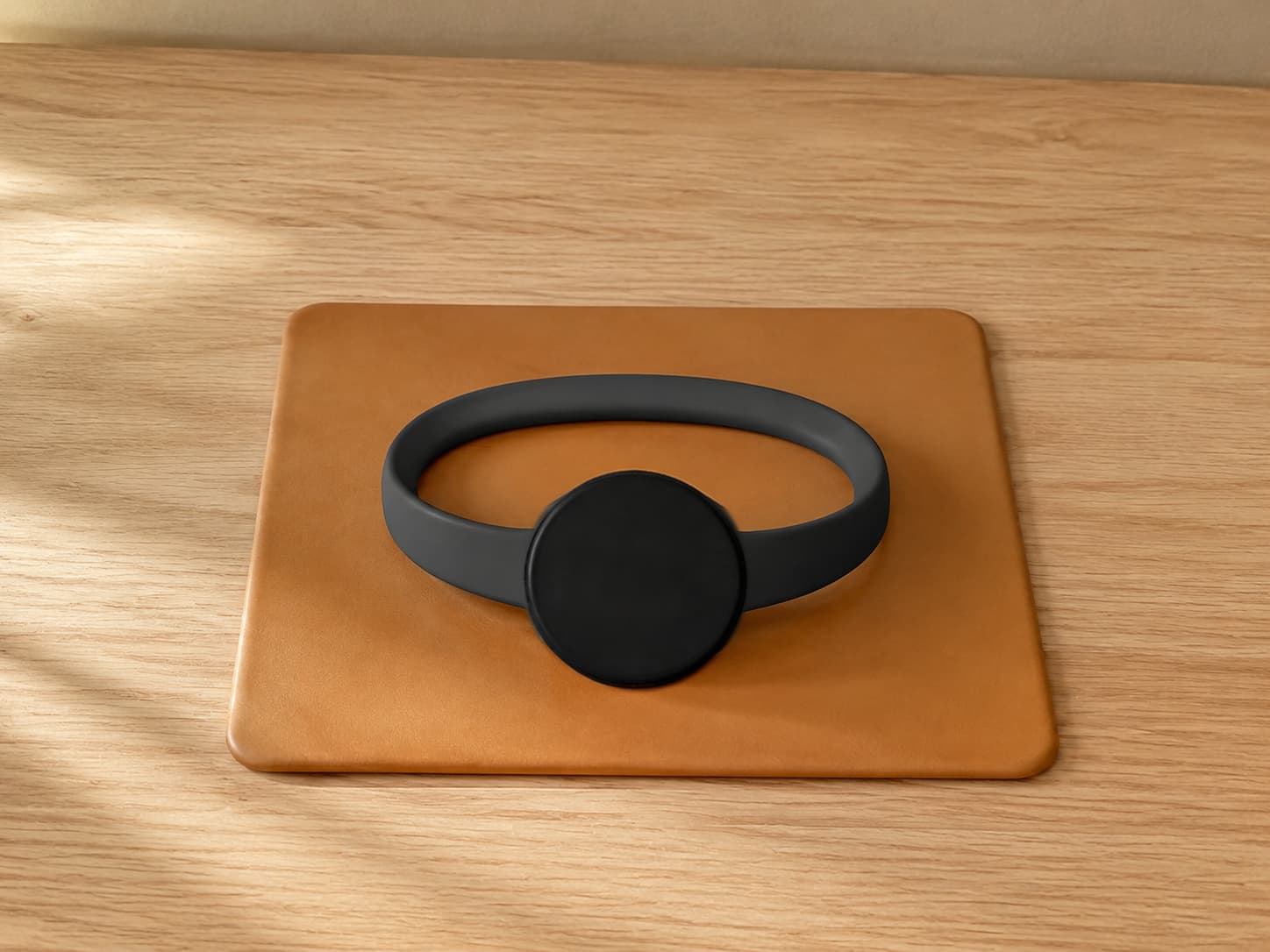 A powered-off black smartwatch with a looped band resting on a tan leather mat on a wooden table.