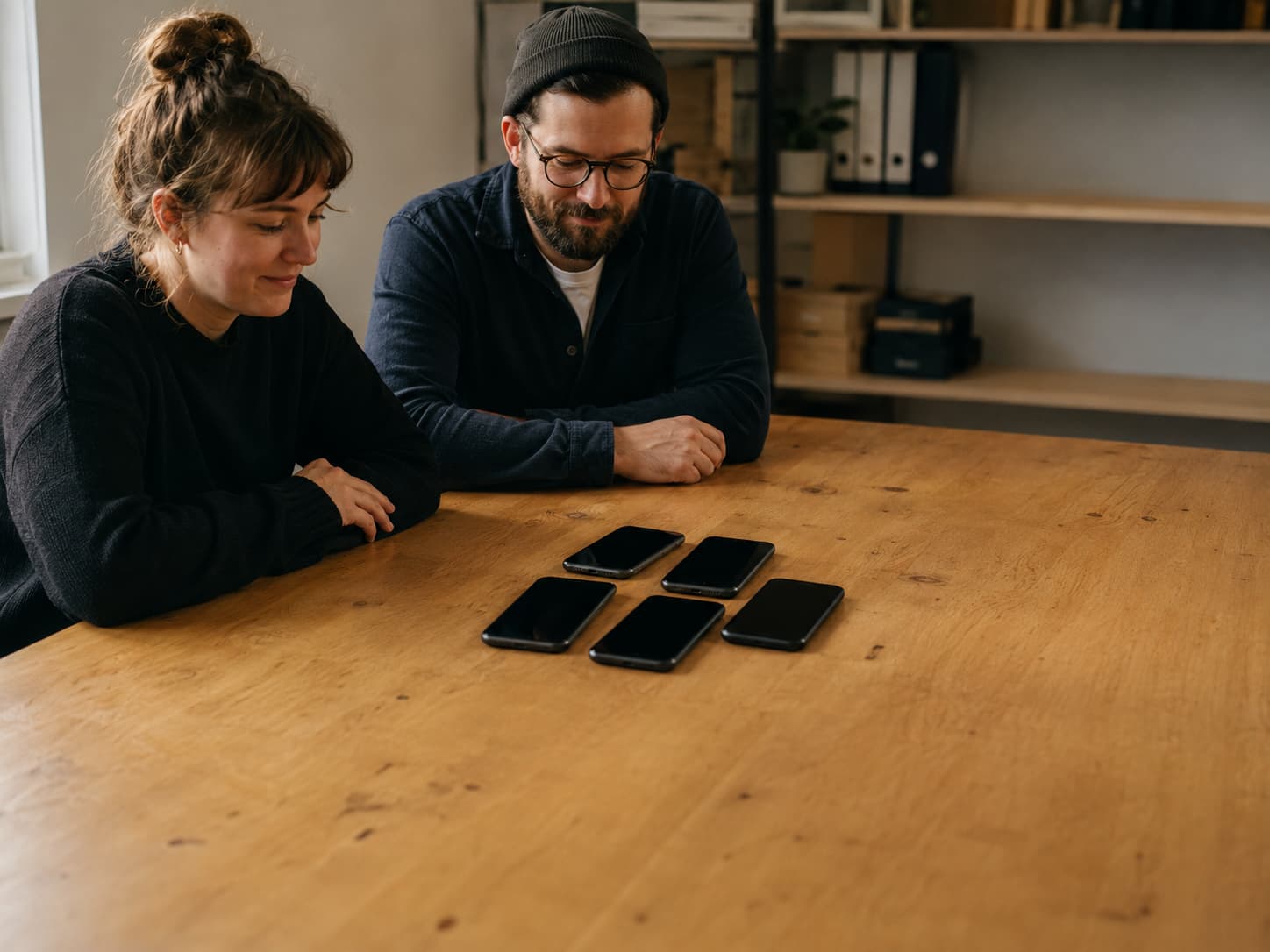 Two colleagues reviewing five powered-off phones grouped on a work table