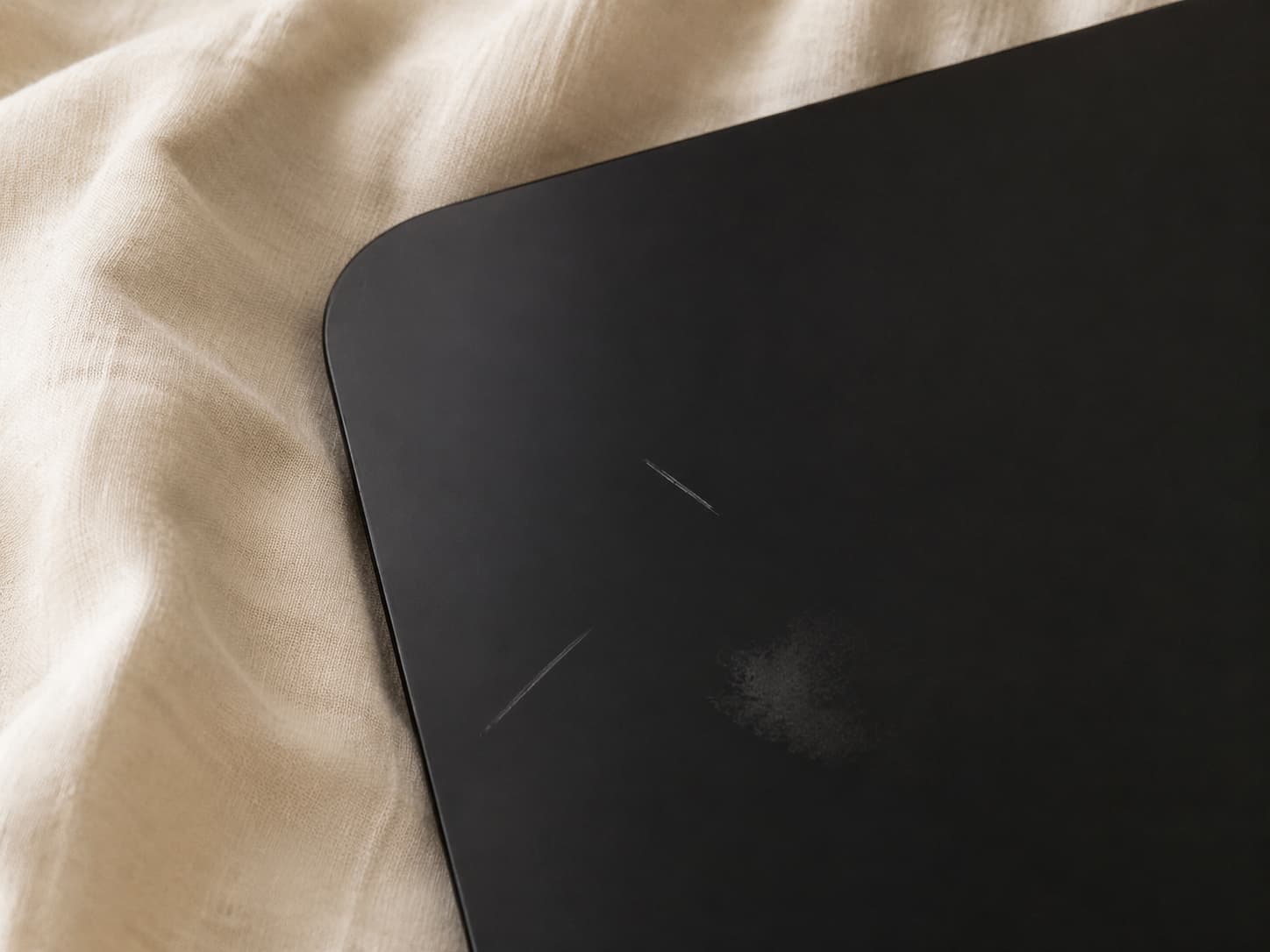 A close view of visible surface scuffs on a dark mobile phone screen resting on cream fabric
